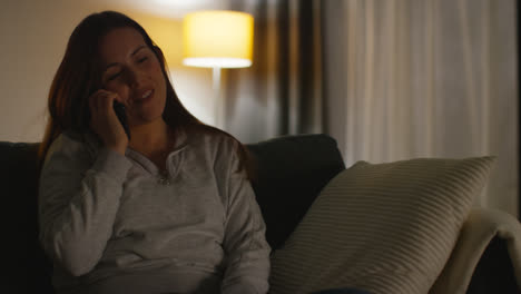 Close-Up-Of-Smiling-Woman-Sitting-On-Sofa-At-Home-At-Night-Talking-On-Mobile-Phone-3